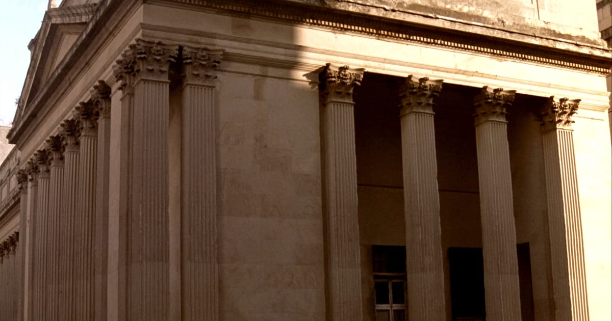 The corner of a neoclassical stone building, its Corinthian columns lit by low sun.