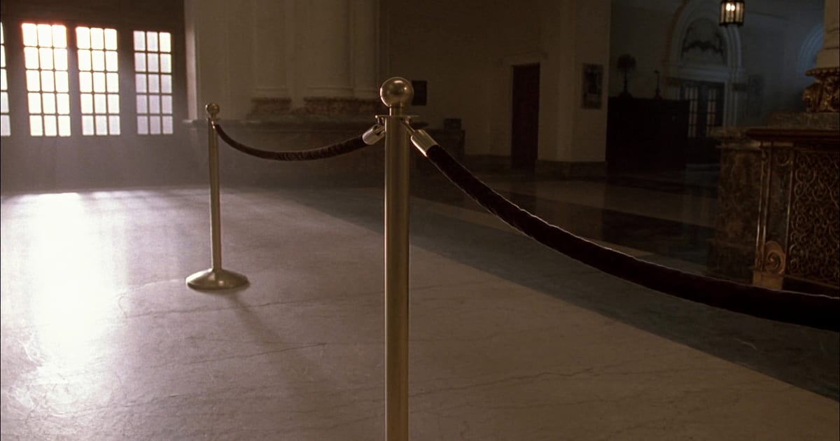 A brass stanchion and rope barrier across the polished floor of an empty marble hall.